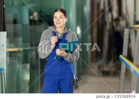 In glass processing workshop, woman works with papers, fills out report In glass processing workshop, woman works with papers, fills out report 135388914