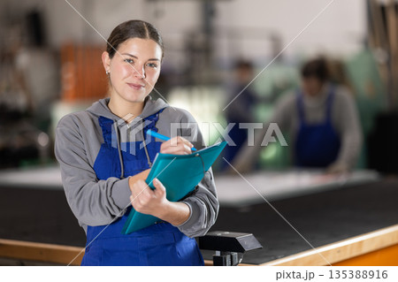 In glass processing workshop, woman works with papers, fills out report 135388916