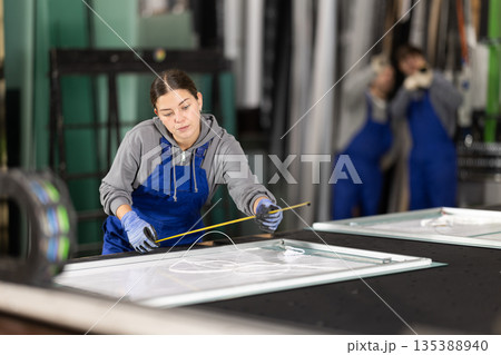Young woman employee in blue overall measures given length of plastic material 135388940