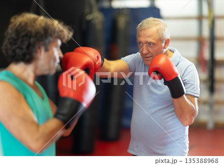 Older man in boxing gloves landing punch in self-defense sparring Older man in boxing gloves landing punch in self-defense sparring 135388968