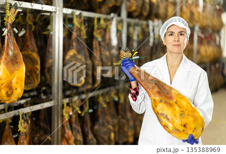 In jamon production shop, woman employee demonstrates final product 135388969