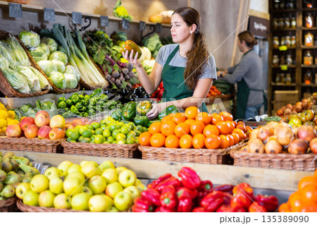 Female seller holding green peppers standing in fruit and vegetable section of supermarket 135389090