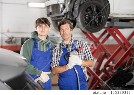 Guy and man mechanics posing in car repair shop Guy and man mechanics posing in car repair shop 135389315