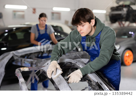 Young auto body technician sanding car bumper with sandpaper Young auto body technician sanding car bumper with sandpaper 135389442
