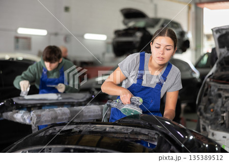 Woman auto mechanic using grinding machine prepares car parts for painting 135389512