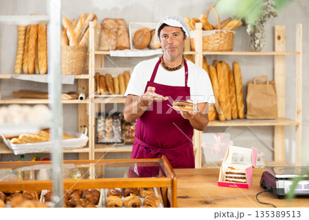 Middle-aged salesman offering a piece of cake in plate in bakery Middle-aged salesman offering a piece of cake in plate in bakery 135389513