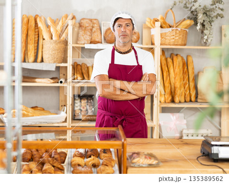 Portrait of friendly baker selling fresh baguettes and croissants in bakery 135389562