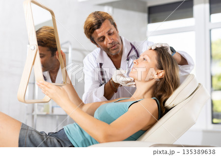 Male beautician giving consultation to woman patient with mirror in aesthetic clinic 135389638
