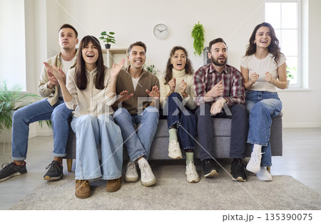 Happy fans watch a tense football game together at home, cheering on the couch 135390075