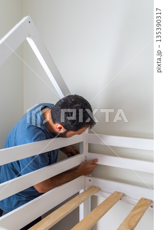 A man is working on a bed frame, possibly fixing it or building it 135390317