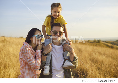 Family enjoying golden meadow walk at sunset, child and parents in nature Family enjoying golden meadow walk at sunset, child and parents in nature 135391447