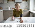 Middle aged woman sits at table measuring blood pressure with tonometer, seasonal health problems. 135391451