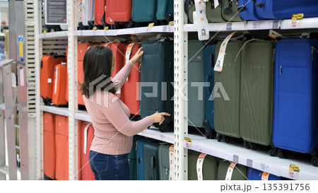 Young female shopper comparing different suitcases in a travel goods section, making luggage choice and vacation planning Young female shopper comparing different suitcases in a travel goods section, making luggage choice and vacation planning 135391756