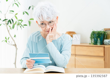 預金通帳を見て考えるシニア女性 135392387