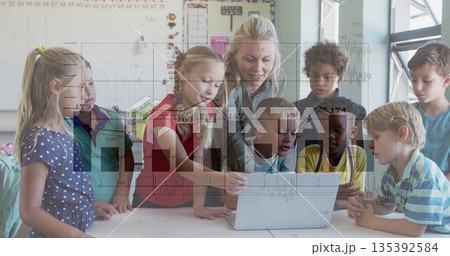 Pointing teacher guiding eight children around laptop on white table in classroom, with whiteboard Pointing teacher guiding eight children around laptop on white table in classroom, with whiteboard 135392584
