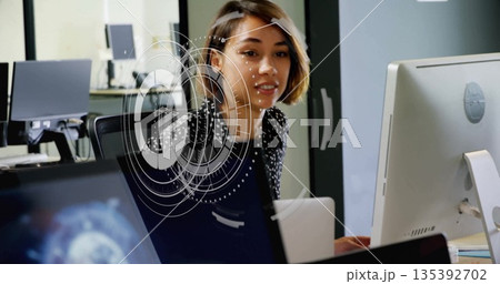 IT professional wearing polka dot blouse analyzing monitors and laptop in office, with AR interface 135392702