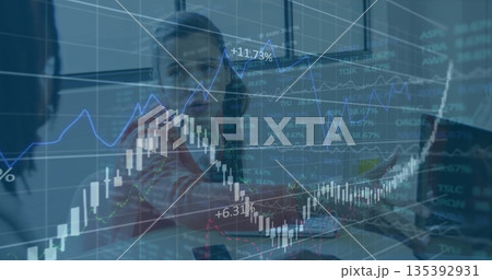 Professionals pointing at stock trends in office, candlestick graphs on translucent screen 135392931