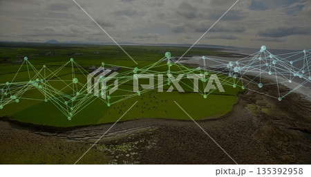 Mapping digital overlay extending over coastal field, with glowing nodes, livestock and rocky shore 135392958