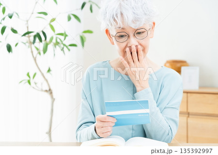 預金通帳を見て考えるシニア女性 預金通帳を見て考えるシニア女性 135392997