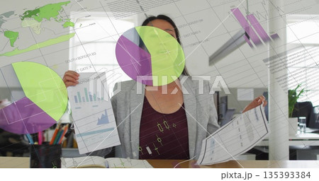 Businesswoman wearing business attire analyzing printed data reports in office, with digital charts Businesswoman wearing business attire analyzing printed data reports in office, with digital charts 135393384