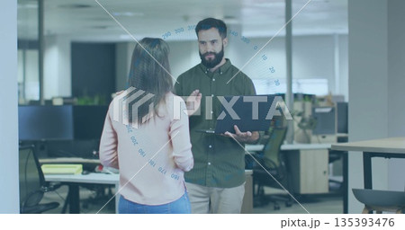 Holding laptop, coworkers wearing business attire discussing project in open plan office 135393476