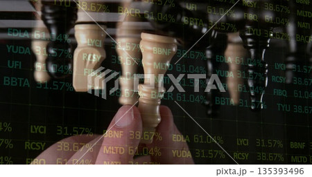 Grasping human hand selecting beige chess piece in dark studio set, with financial ticker overlay Grasping human hand selecting beige chess piece in dark studio set, with financial ticker overlay 135393496