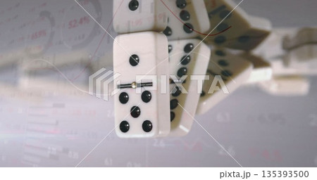 Falling white domino tiles cascading in studio, with faint data charts with percentage labels 135393500