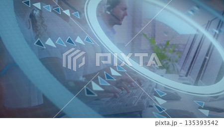 Typing agents wearing headsets at open-plan office desk with keyboards, plant and network overlay 135393542