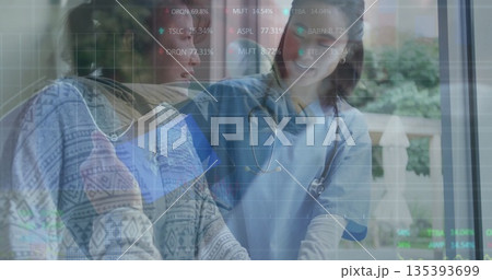 Patient in patterned sweater and doctor reviewing digital display at clinic table with stethoscope 135393699