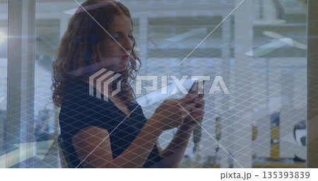 Woman holding smartphone, standing near wire mesh glass wall at lobby with benches and tables Woman holding smartphone, standing near wire mesh glass wall at lobby with benches and tables 135393839