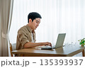 Happy young Asian man working on laptop in living room 135393937