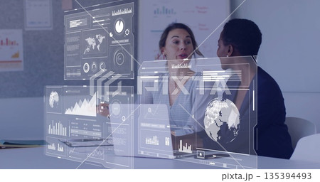 Two analysts reviewing data in formal wear at conference table, using laptop, phone, digital charts Two analysts reviewing data in formal wear at conference table, using laptop, phone, digital charts 135394493