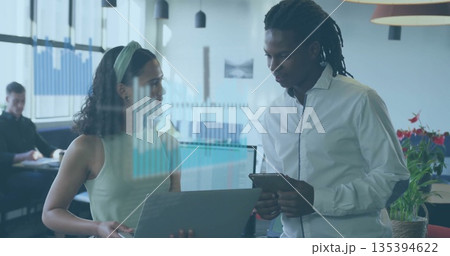 Collaborating woman in green top and man in white shirt using laptop and tablet in office 135394622