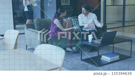 Discussing Indian woman and white man sitting on gray sofa at corporate lounge, with tablet laptop Discussing Indian woman and white man sitting on gray sofa at corporate lounge, with tablet laptop 135394639