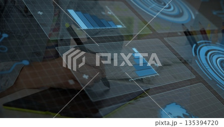 Hand holding stylus pen drawing visualizations on office desk, with coffee mug and floating charts 135394720