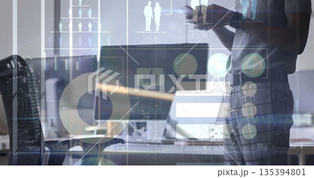 Holding smartphone worker standing beside desk in office with laptop-monitor and graphs, copy space Holding smartphone worker standing beside desk in office with laptop-monitor and graphs, copy space 135394801