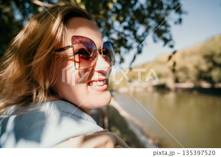 Smiling Woman in Sunglasses with a View of a Lake 135397520
