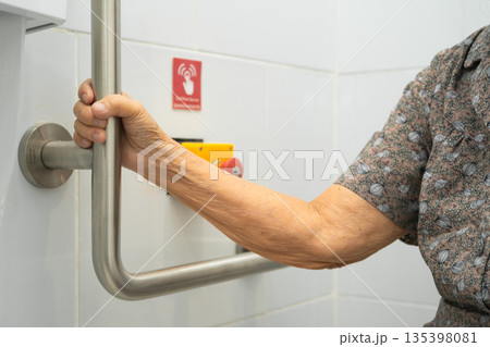 Asian elderly woman use toilet security support rail in bathroom. Asian elderly woman use toilet security support rail in bathroom. 135398081