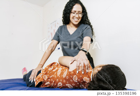 Woman doing shoulder rehabilitation physiotherapy. Physiotherapist rehabilitating shoulder to patient lying on her side. Shoulder and back treatment and rehabilitation concept 135398196