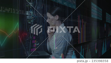 Analyzing woman in blazer reviewing financial charts in data center, with laptop and cables 135398358