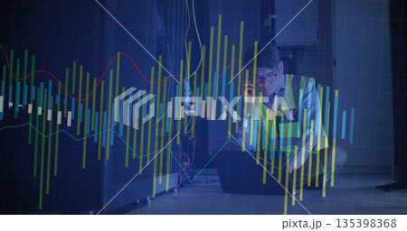 Crouching Korean engineer in safety vest checking laptop and phone in server room with rack, charts Crouching Korean engineer in safety vest checking laptop and phone in server room with rack, charts 135398368