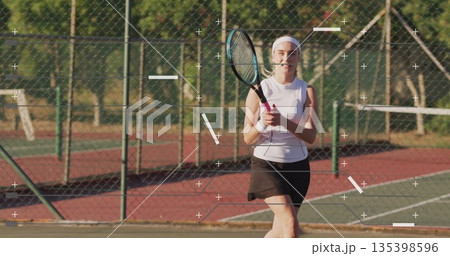 Preparing tennis player in white top gripping racket on painted park court, with chainlink fence Preparing tennis player in white top gripping racket on painted park court, with chainlink fence 135398596