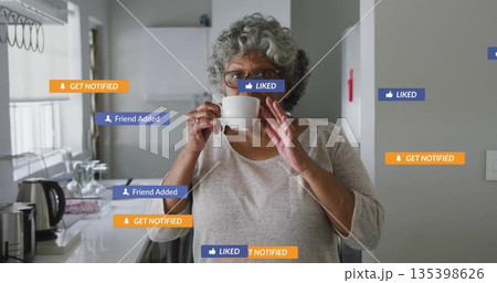 Senior woman sipping from white ceramic mug in home kitchen, with digital notification icons Senior woman sipping from white ceramic mug in home kitchen, with digital notification icons 135398626