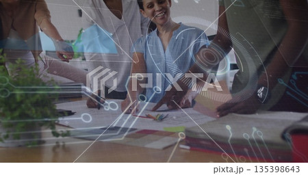 Leaning women pointing, discussing design sketches in office meeting, with digital overlay 135398643