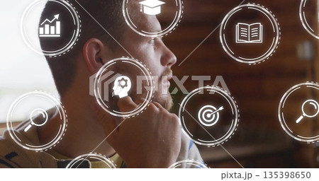 Contemplating man resting hand on chin at office desk, with floating digital interface icons 135398650