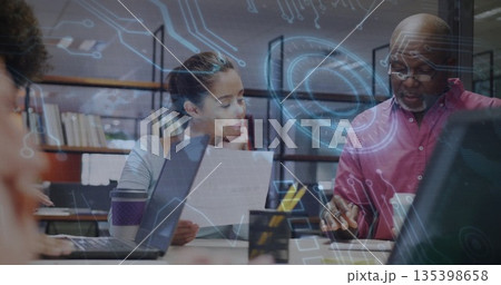 Collaborating woman and senior man examining document at conference table with laptops, overlays 135398658