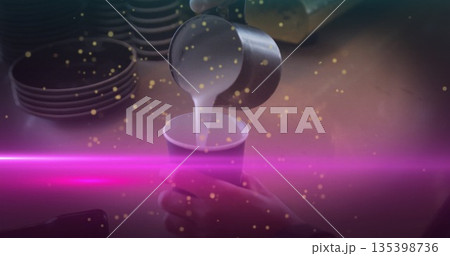 Pouring barista hand guiding metal pitcher filling paper cup at cafe counter, with neon pink light 135398736