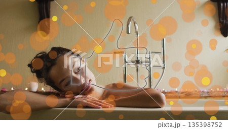 Leaning adult woman resting on porcelain bathtub edge in home bathroom, with tealight candles 135398752