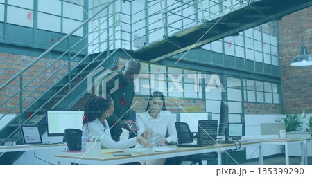 Reviewing papers three coworkers in business attire leaning over desk in loft office, with laptops 135399290