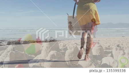 Mother and children walking and playing in oceanfront sand by surf, with sandcastles and beach ball Mother and children walking and playing in oceanfront sand by surf, with sandcastles and beach ball 135399336